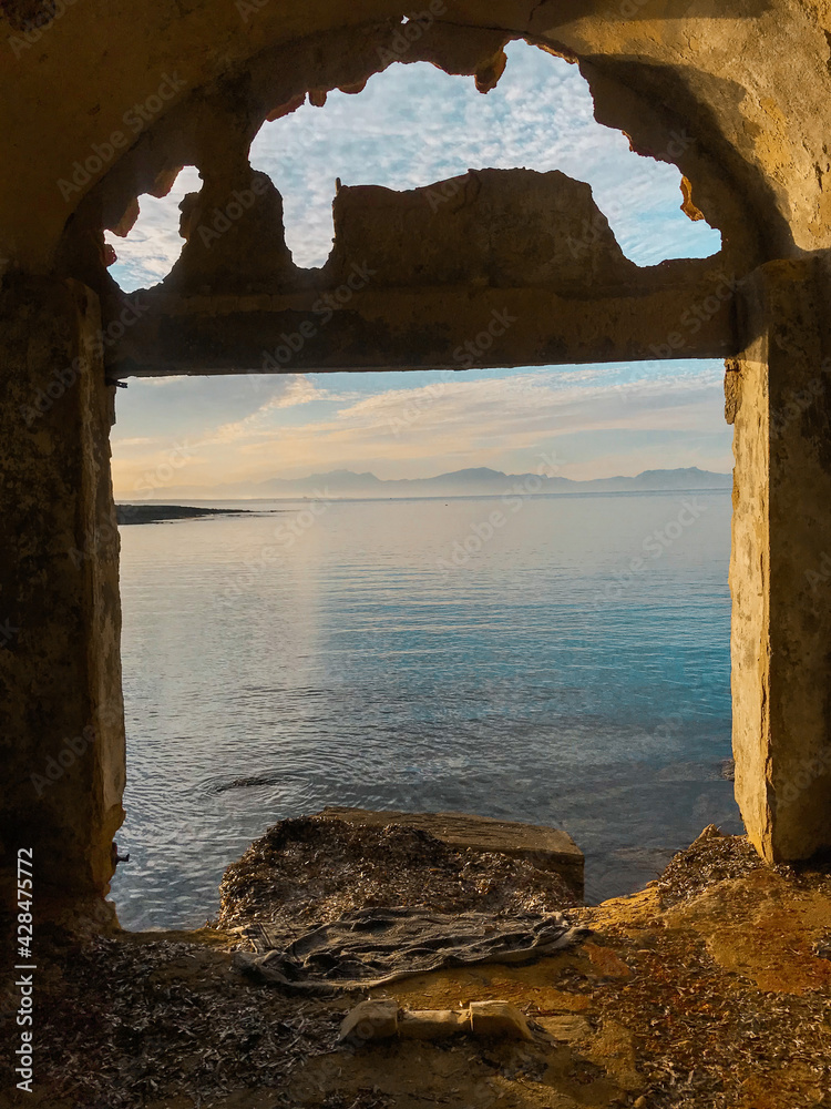 Embarcadero en ruinas con agujeros donde se observa el mar azul calmado y en el horizonte montañas un dia soleado con nubes en Mallorca