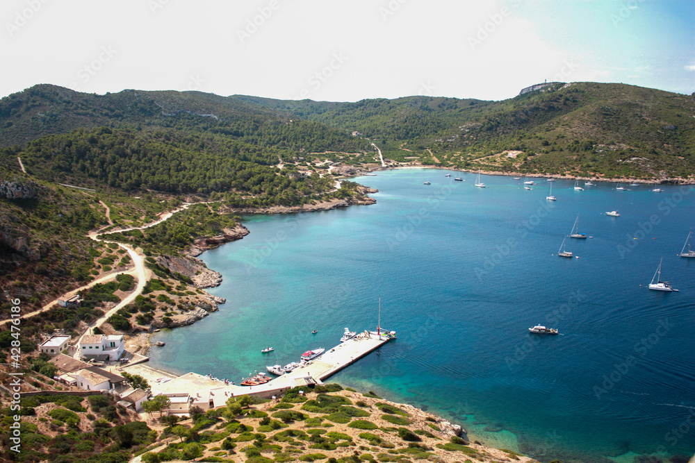 Bahia de Cabrera, mar calmado un día de verano con varios barcos y pequeñas montañas con caminos de tierra