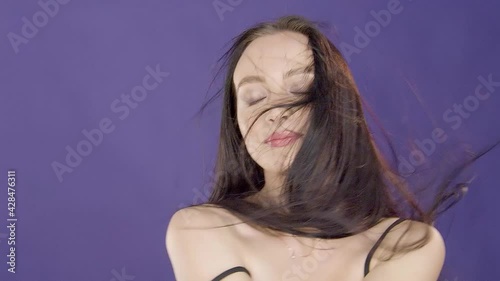 Charming beautiful cute young girl brunette model with beautiful eyes poses for camera and touches wind blowing hair on purple background in foto studio