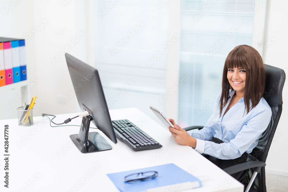 Woman using her tablet in front of her desktop computer Woman using her tablet in front of her desktop computer