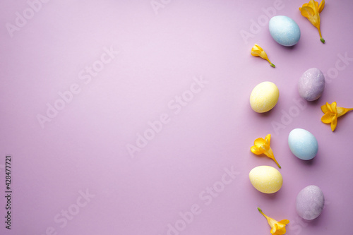 Easter eggs and freesia flowers on a purple background, place for text. Flat lay.