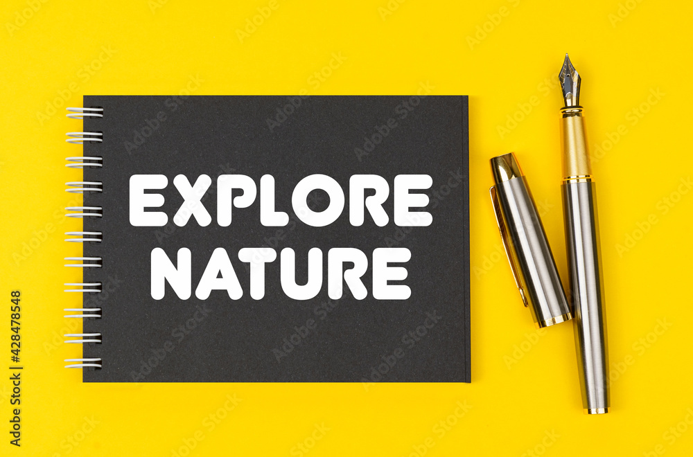 On a yellow background lies a pen and a black notebook with the inscription - Explore Nature On a yellow background lies a pen and a black notebook with the inscription - Explore Nature