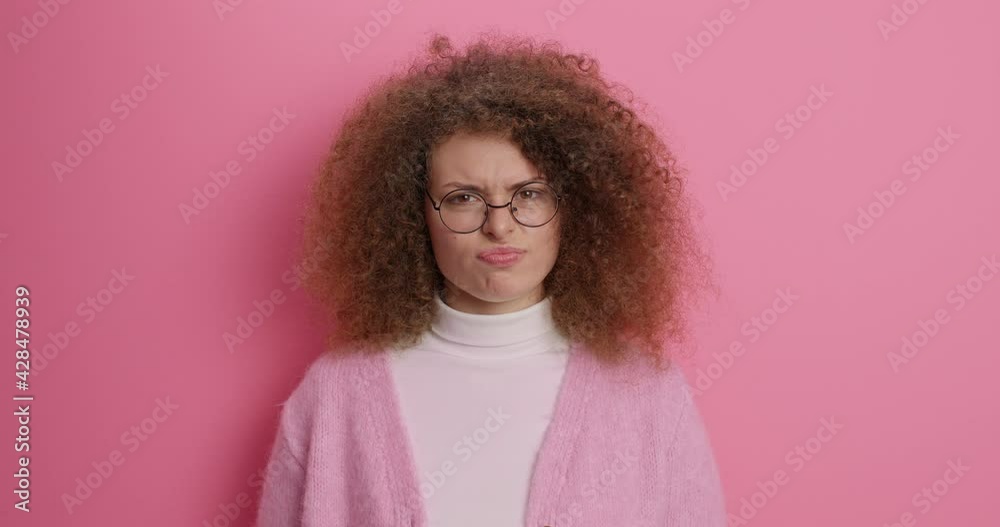Unhappy dissatisfied woman smirks face shakes head doesnt like suggestion looks discontent says no I dont agree wears round spectacles and jumper isolated over pink background. Human reaction Unhappy dissatisfied woman smirks face shakes head doesnt like suggestion looks discontent says no I dont agree wears round spectacles and jumper isolated over pink background. Human reaction