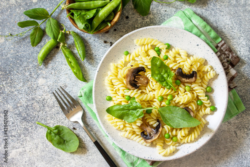 Healthy eating. Pasta fusilli with mushrooms, spinach and green peas on stone table. Vegetarian vegetable mushrooms pasta. Diet menu. Top view flat lay.