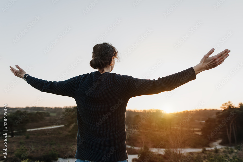 Motivated, cheerful person with outstretched, open arms in beautiful, relaxing nature. Woman feels freedom, motivation and has goals in life.