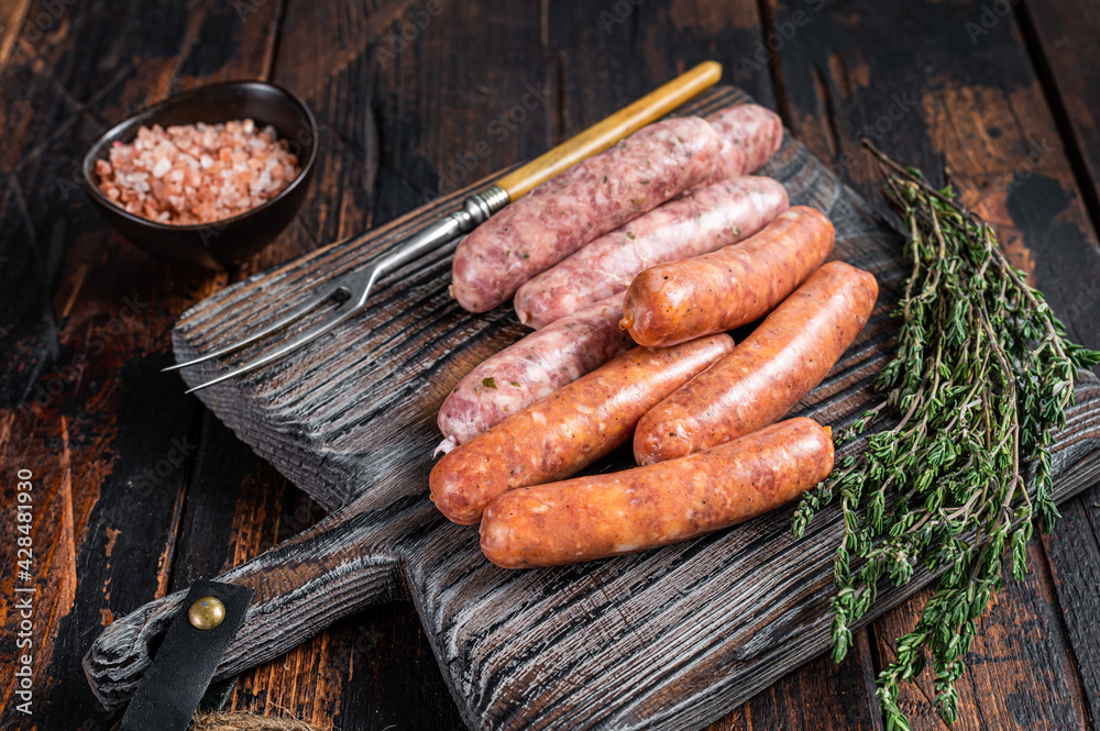 Assorted Raw pork and beef sausages with spices on a wooden board with thyme. Dark wooden background. Top View