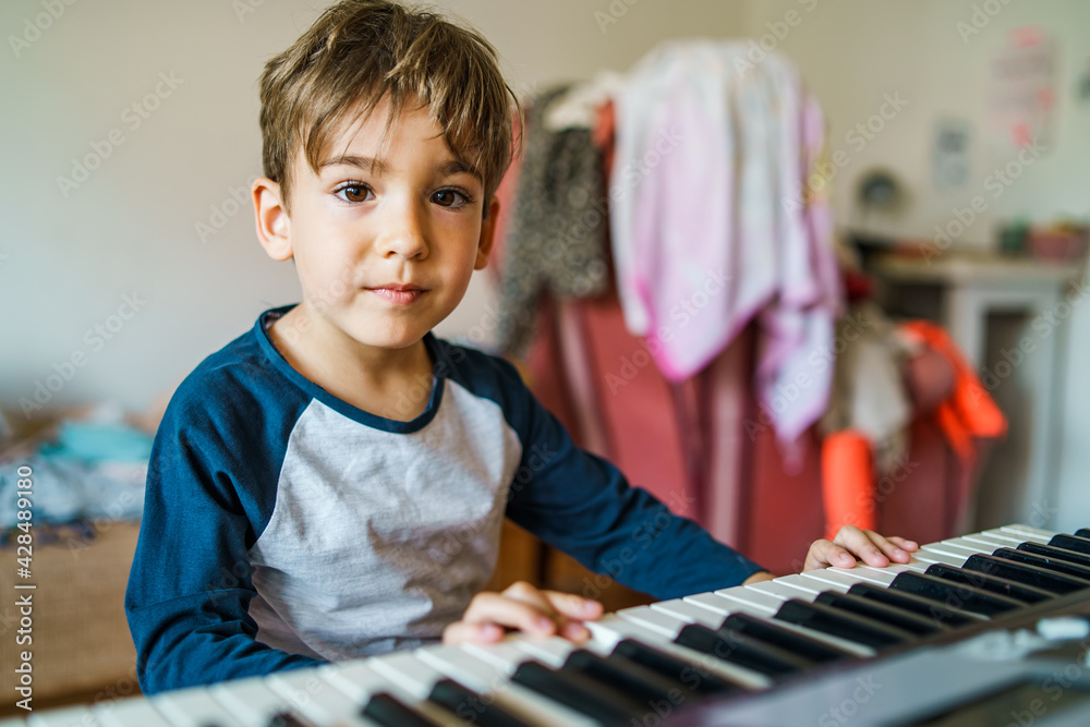 Small caucasian boy playing electric piano making music at home leisure activity growing up education and art concept playful child having fun at home alone looking to the camera copy space Small caucasian boy playing electric piano making music at home leisure activity growing up education and art concept playful child having fun at home alone looking to the camera copy space