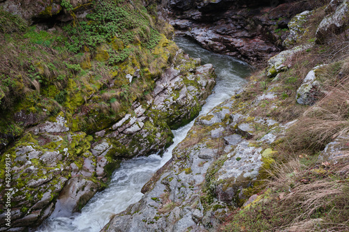 Powerful mountain river flowing through the narrow canyon with colorful, wet cliffs covered by vivid moss, grass and flowers at early spring photo