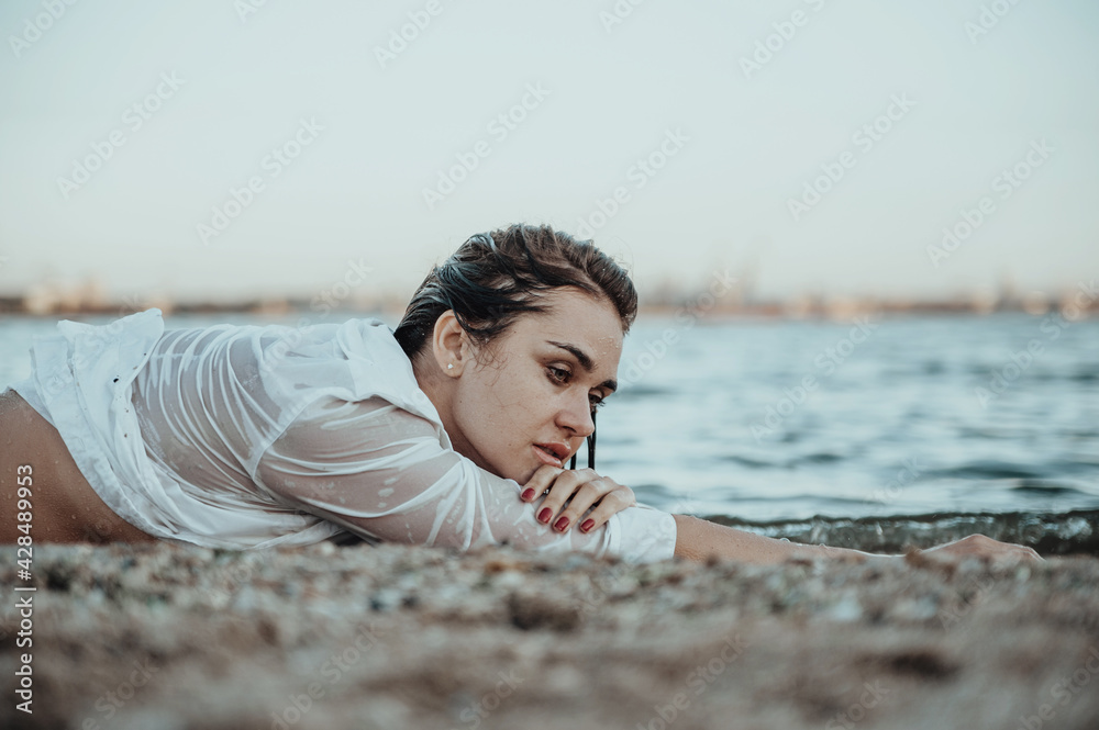 Beautiful woman in white shirt posing on the beach. Young beautiful woman posing at sunset. Summer time concept.