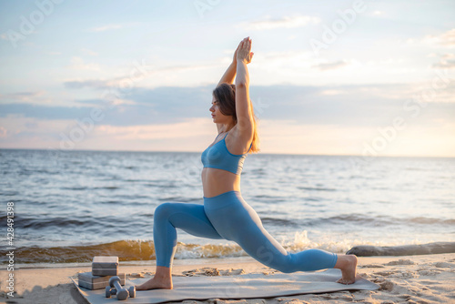 sportive athletic woman practices yoga on the beach. young woman performs assana. workout outdoors  sports. healthy lifestyle concept. space for text