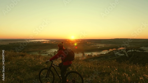 Fototapeta Naklejka Na Ścianę i Meble -  The silhouette of a cyclist traveler rides along the edge of the mountain, admiring the landscape and the sunrise. Free tourist rides a bike in nature in the sun. Sports lifestyle. Cyclist exercising