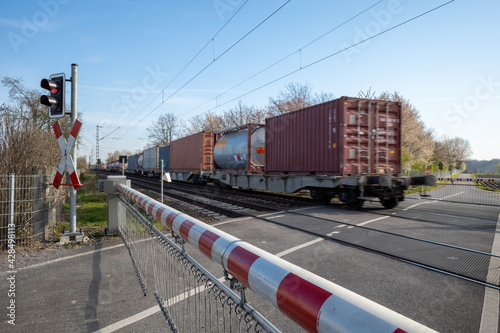 Fotografie Selective focus view at red and white level crossing railway barrier which block the road and locomotive of freight train move on the rail on countryside in Germany