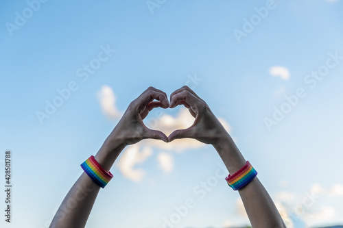 woman hands showing heart figure with gay pride bracelets