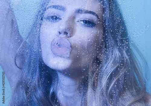 Fototapeta Naklejka Na Ścianę i Meble -  Sexy woman in bodysuit in blue studio kiss over wet glass.