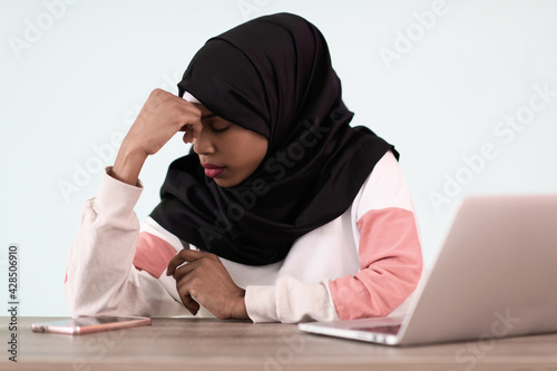 afro girl wearing a hijab is disappointed and sad sitting in her home office and using a laptop