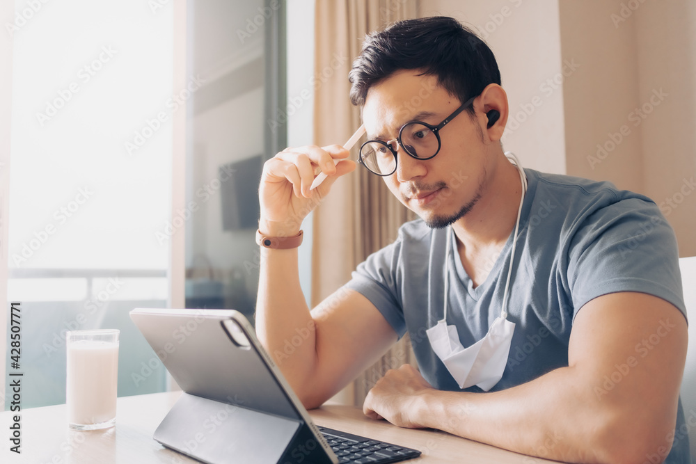 Happy Asian man is working on his tablet in concept of work from home. Happy Asian man is working on his tablet in concept of work from home.