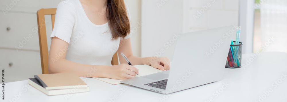 Young asian woman writing on notebook for planning working and using laptop computer on desk at home, girl notes about finance, female study and learning, business and communication concept. Young asian woman writing on notebook for planning working and using laptop computer on desk at home, girl notes about finance, female study and learning, business and communication concept.