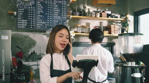 Asian Waitress taking order from telephone for take away curbside and delivery order. Barista waiter use tablet and telephone take order from customer in coffee shop.