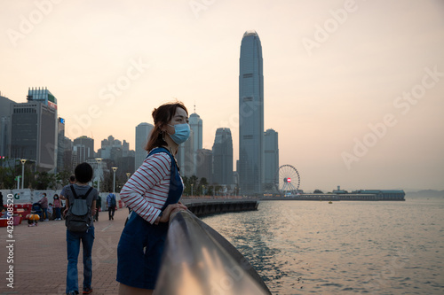asian young lady with face mask, Colorful magnificent sunset city view of Central, Victoria Harbour, Hong Kong in background