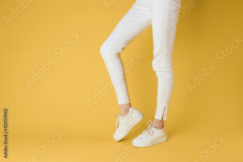 Female feet white sneakers attractive look fashion yellow background