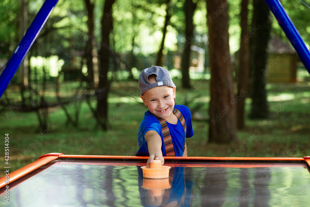 happy little boy playing a air hockey in the park wearing a cap and blue t-shirt happy little boy playing a air hockey in the park wearing a cap and blue t-shirt