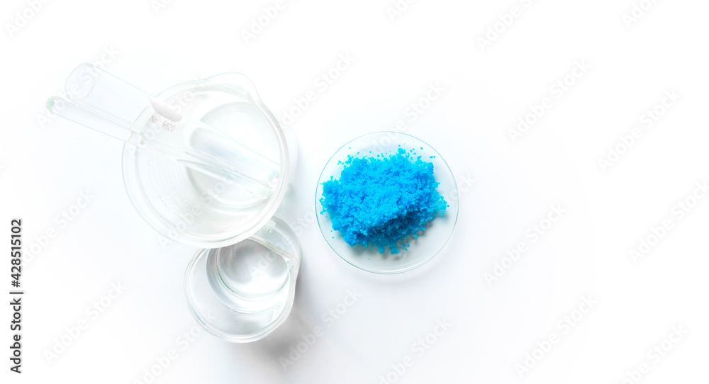 Copper(II) sulfate in Chemical Watch Glass, test tube, Stirring Rod and alcohol in beaker place on white laboratory table. Top view Copper(II) sulfate in Chemical Watch Glass, test tube, Stirring Rod and alcohol in beaker place on white laboratory table. Top view