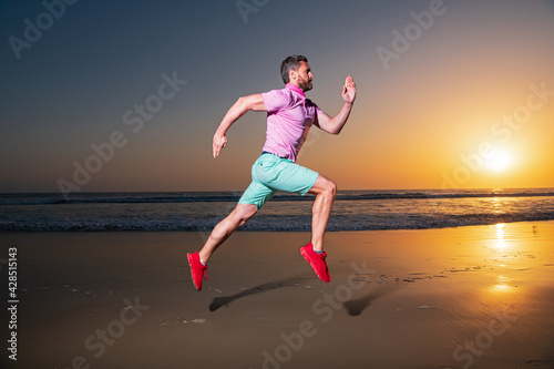 Man running on the beach at sunset. Guy runner jogger running. Dynamic jumping movement. Sport jump.
