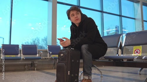 Young businessman waiting for delayed flight airplane in airport modern waiting room crowded with passengers.