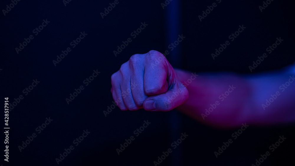 Close up of a male clenched fist in a dark room lighting.