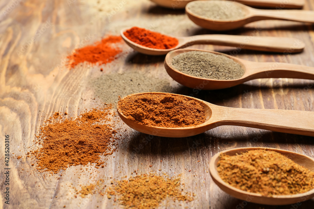 Spoons with different spices on wooden background, closeup