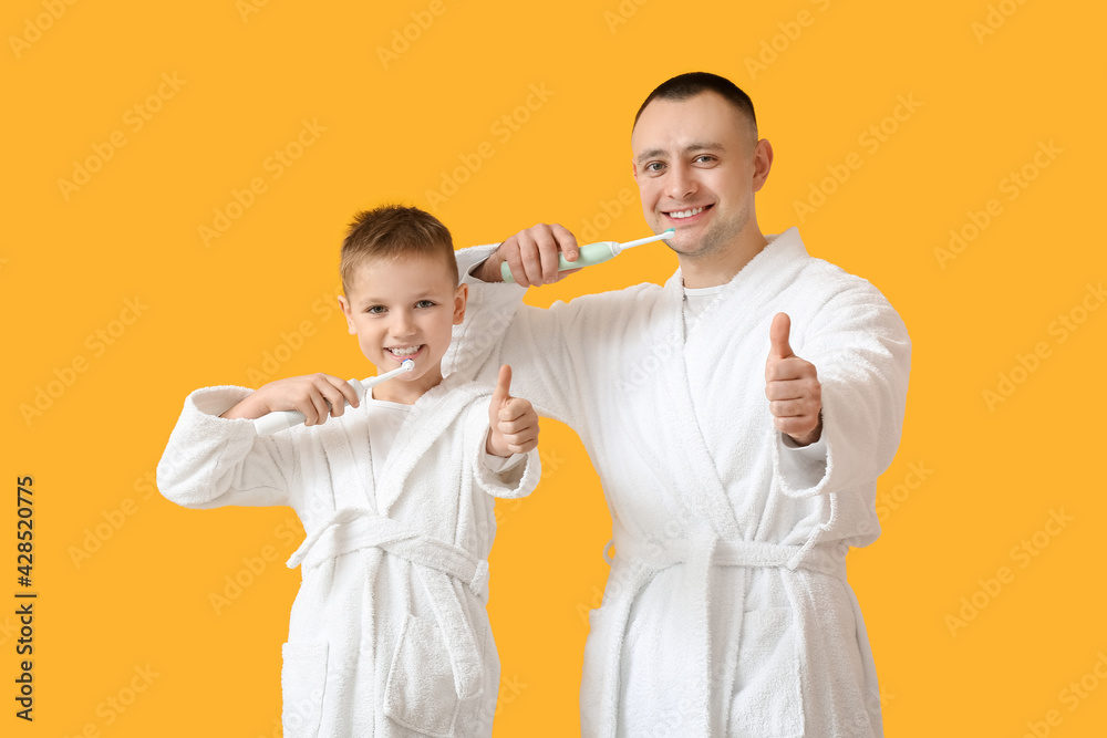Father with little son brushing teeth and showing thumb-up on color background