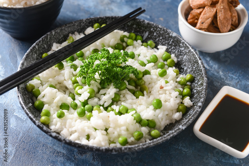 Plate with tasty rice and green peas on color background