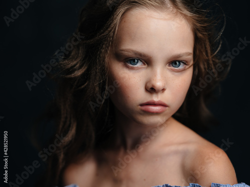 A beautiful blue-eyed girl with bare shoulders on a dark background and curly hair