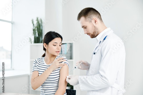 male doctor in a white coat injections in the shoulder of a woman patient covid vaccination