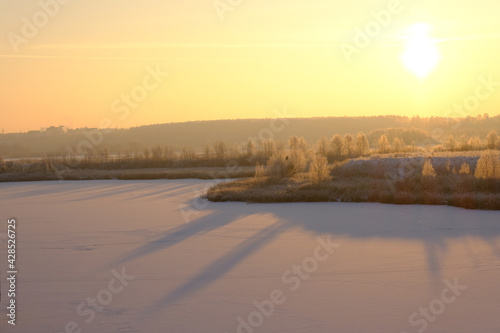 Winter sunset in nature. The snow-covered surface of the lake, trees and bushes.
