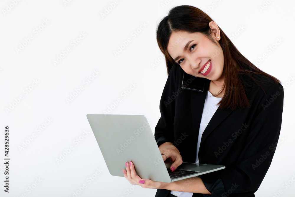 Asian beautiful business woman wearing formal black suit, smiling with happiness, typing and using laptop for working while talking or communicating on mobile phone with isolated white background. Asian beautiful business woman wearing formal black suit, smiling with happiness, typing and using laptop for working while talking or communicating on mobile phone with isolated white background.