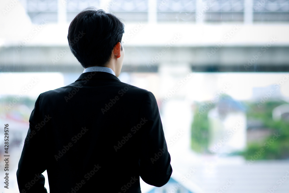 A Business man wearing formal black suit, turn back, standing and looking outside the window. Presenting about future and vision of successful leadership. A Business man wearing formal black suit, turn back, standing and looking outside the window. Presenting about future and vision of successful leadership.