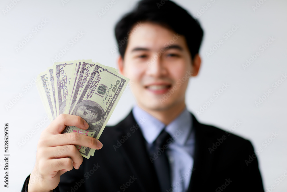 Selective focus on holding dollar bank notes or money with blur background of asian smiley business man. Financial Concept. Selective focus on holding dollar bank notes or money with blur background of asian smiley business man. Financial Concept.