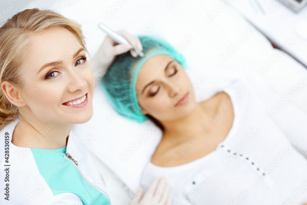 Fototapeta premium Professional beautician doing eyebrow tattoo at woman face. Permanent brow makeup in beauty salon, closeup. Cosmetology treatment