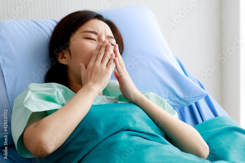 An asian young beautiful female patient getting sick and fever, having sore throat and coughing while lying on bed in hospital. Medical Treatment and Health concept.