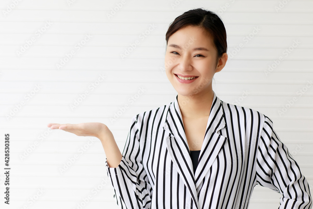 Portrait of an Asian beautiful business woman wearing casual striped pattern shirt, smiling with confidence, show her hand to present blank space and looking to the camera. Portrait of an Asian beautiful business woman wearing casual striped pattern shirt, smiling with confidence, show her hand to present blank space and looking to the camera.