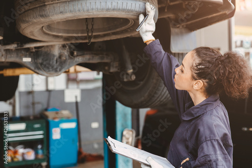 Woman garage worker maintenance checklist at automobile service center, Female in auto mechanic car technician work service check and repair customer car, inspecting car under hood