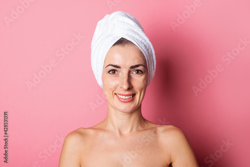 smiling young woman with towel on head, nude shoulders on pink background