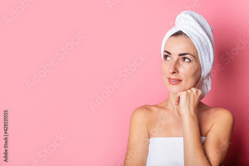 girl with a towel on her head looks to the side on a pink background