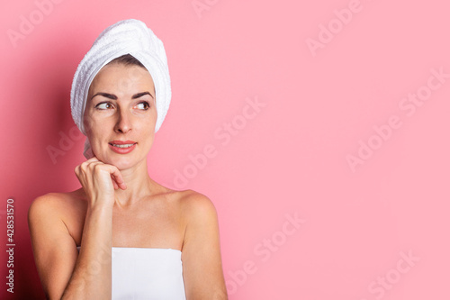 young woman with a towel on her head looks to the side on a pink background