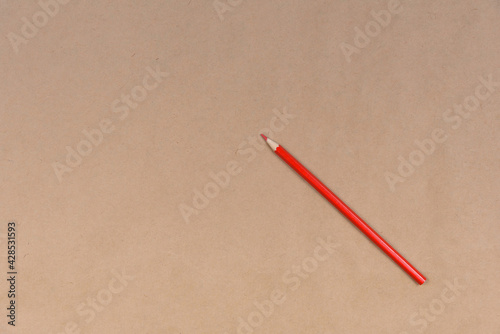 One red pencil lies on craft paper.