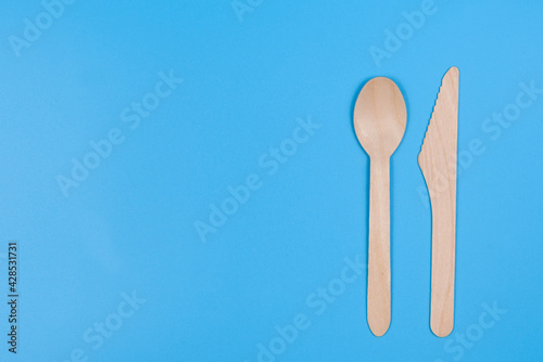Disposable spoon and knife made of wood on a blue background.