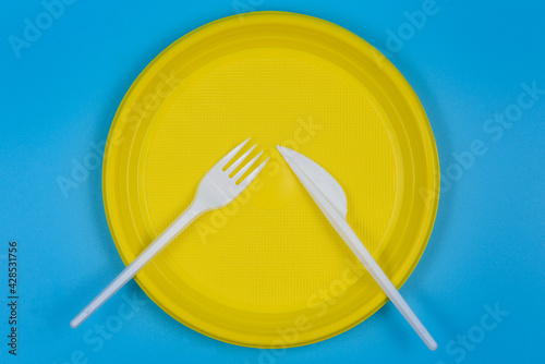 Disposable plate, knife and fork on a blue background.