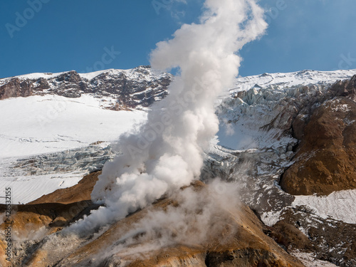 Climbing Mutnovsky volcano. View of the snow-capped mountains of the Mutnovsky volcano and the steam emanating from the fumaroles against the background of the blue sky. Kamchatka Peninsula, Russia.