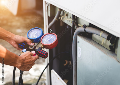 Air repair mechanic using measuring equipment for filling industrial factory air conditioners.	 photo